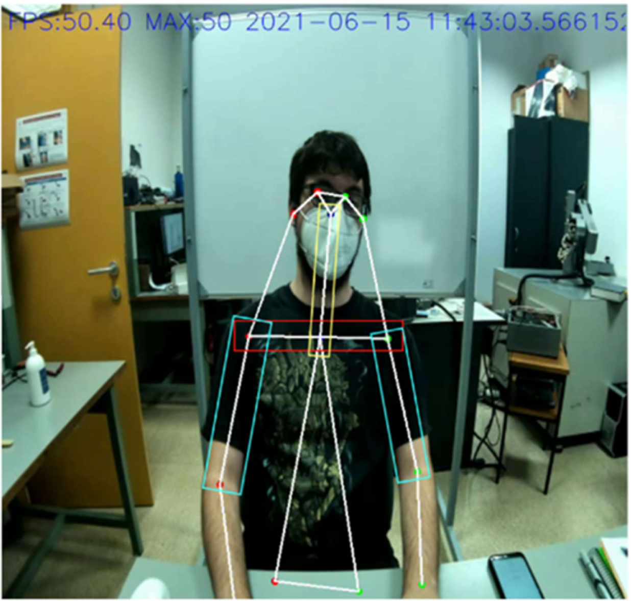 A photograph of a person seated at a desk with posture detection markers on their body, surrounded by office equipment and a whiteboard.